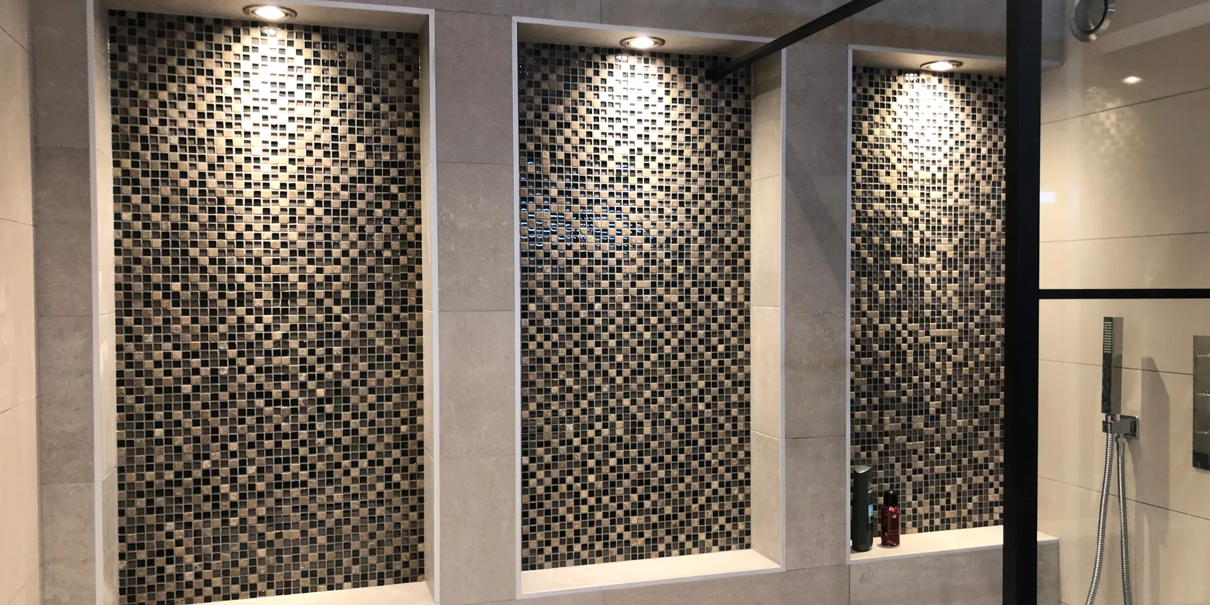 Badkamer in Barendrecht met drie verlichte mozaïeknissen en een zwart omlijste douchewand