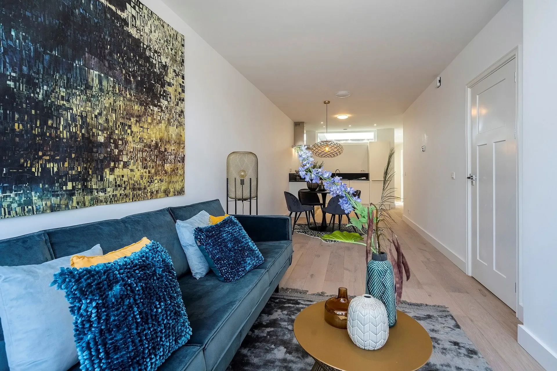 Lange woonkamer met blauwe fluwelen bank en doorkijk naar de gang na een binnenrenovatie