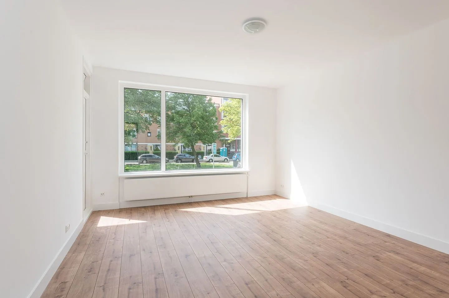 Lichte gerenoveerde woonkamer met groot raam en eikenhouten vloer in een Rotterdams appartement