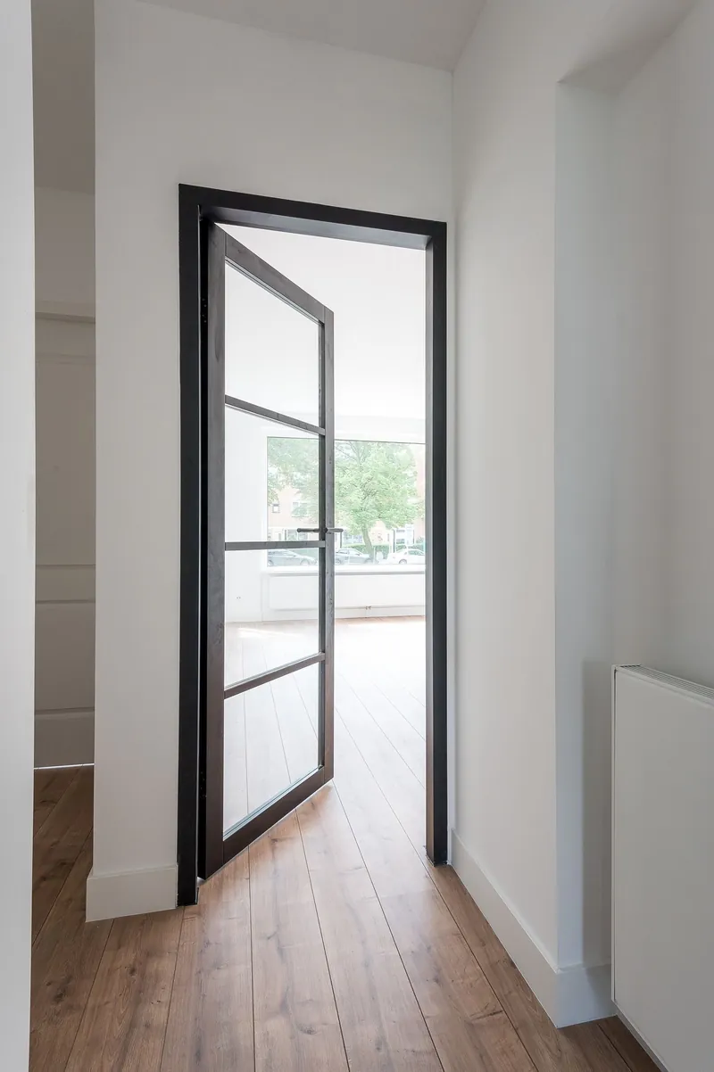 Zwarte stalen taatsdeur met glas in een witte hal van een Rotterdams appartement