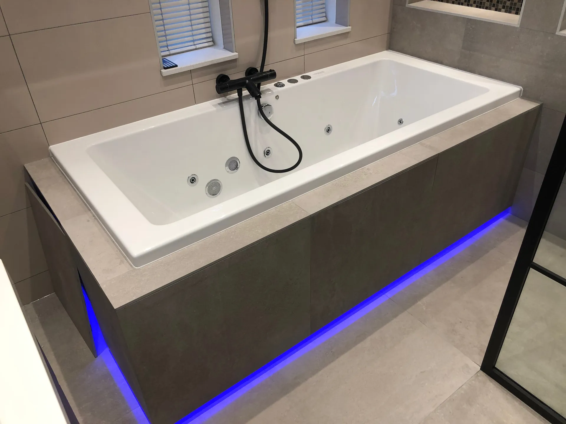 Whirlpoolbad met zwarte kranen en blauwe ledverlichting in een badkamer in Barendrecht