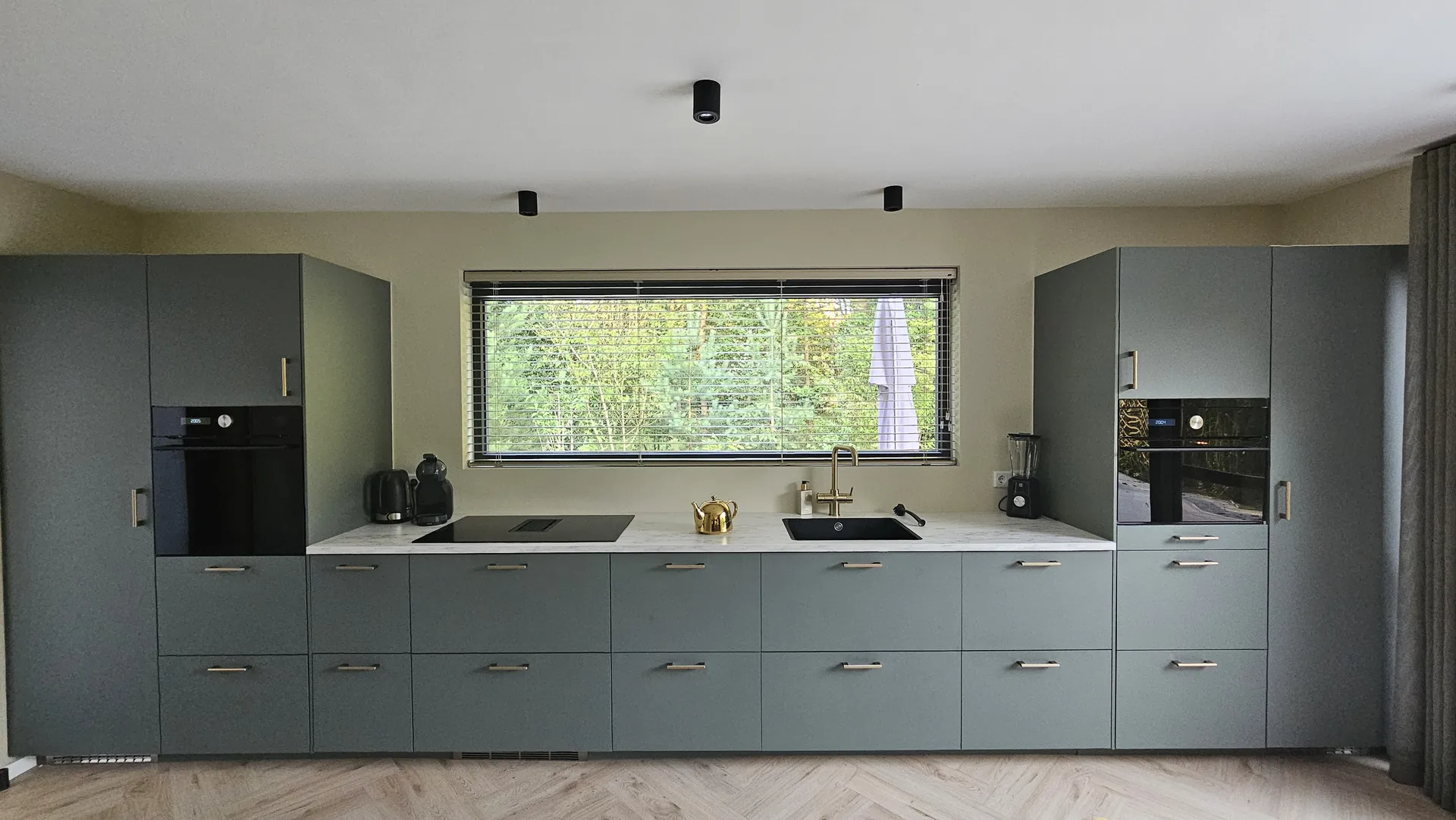 Saliegroene keuken met inbouwapparatuur na de renovatie van een woning in Essen